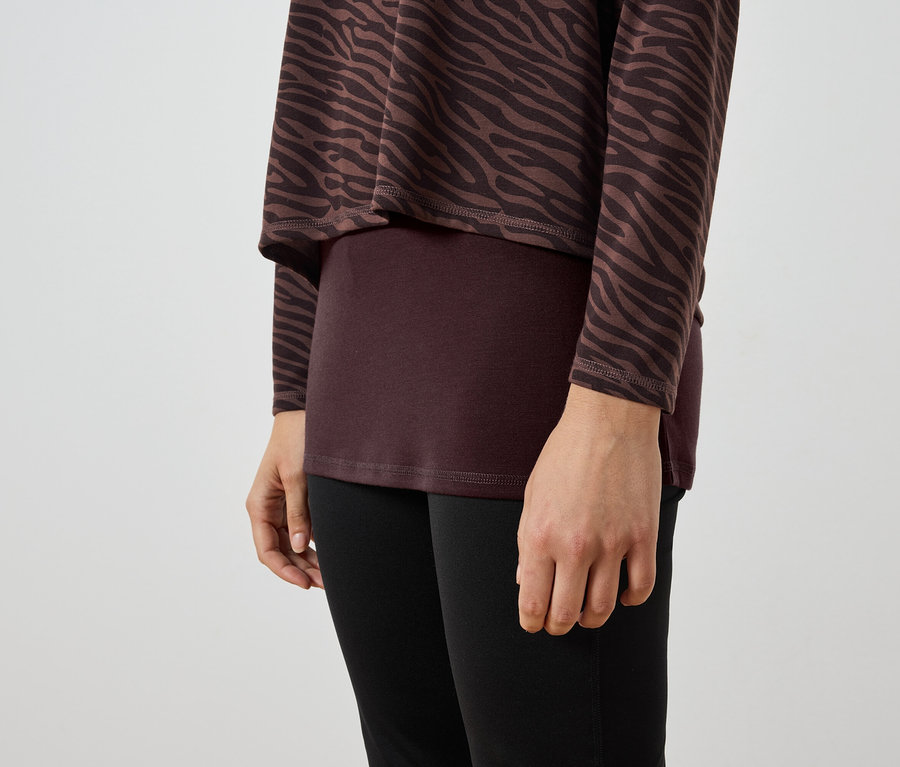 Detailaufnahme einer Frau, die eine braun-schwarze Zebra-Tunika, ein weinrotes Top und schwarze Leggings trägt.