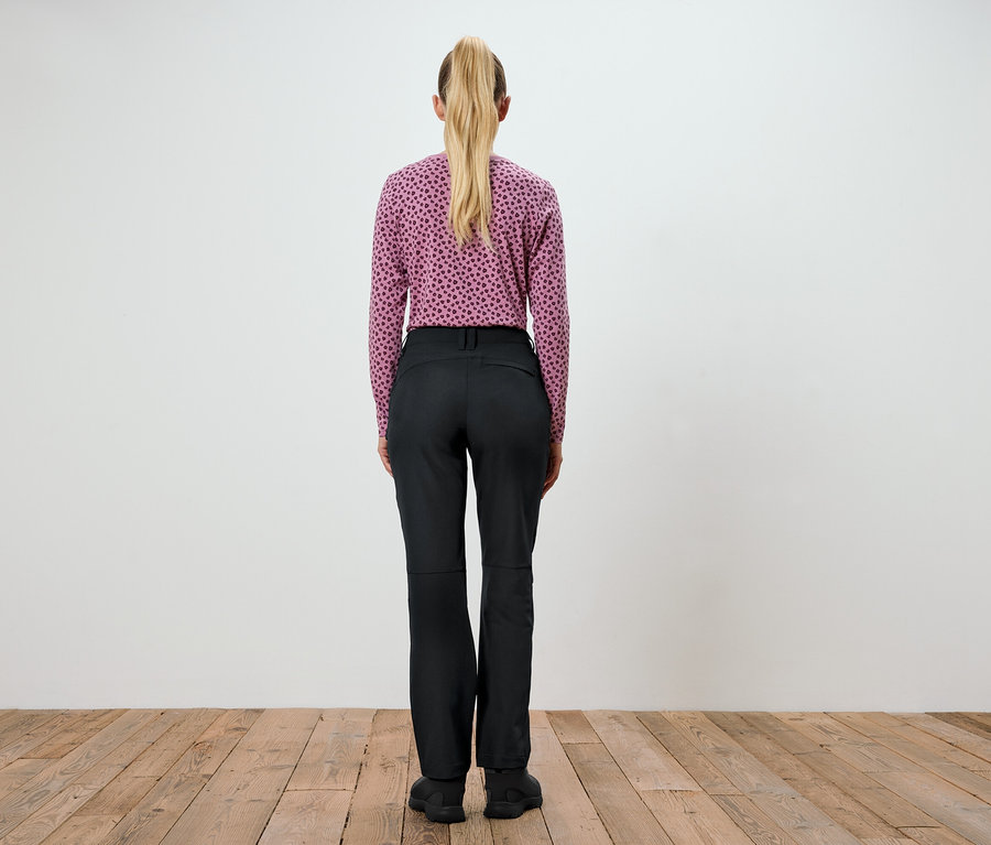Frau steht mit dem Rücken zur Kamera und trägt ein violettes Oberteil mit Aufdruck und eine schwarze Hose.