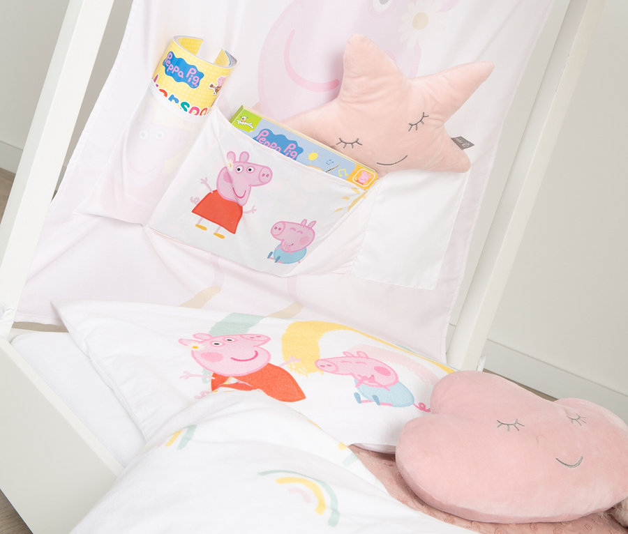 Nahaufnahme eines Kinderbettes mit Peppa Pig-Motiven, darunter ein Buch, ein Becher und Kissen in Stern- und Wolkenform.