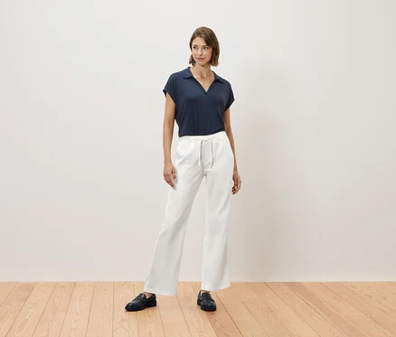 Eine Frau steht auf einem Holzboden und trägt ein marineblaues T-Shirt und eine weiße Hose.