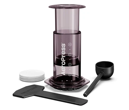 Nahaufnahme eines Aeropress Kaffeebereiters mit Zubehör, inklusive Kaffeelöffel, Rührstab und Papierfilter.