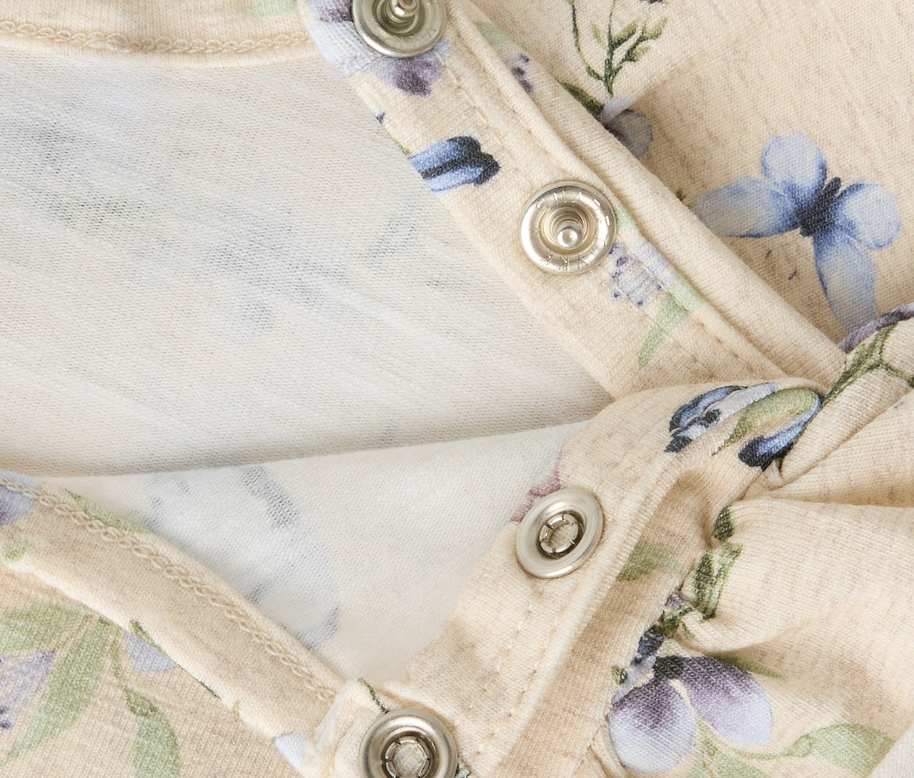 Nahaufnahme des NAME IT Babykleids mit Blumenmuster und Druckknöpfen.