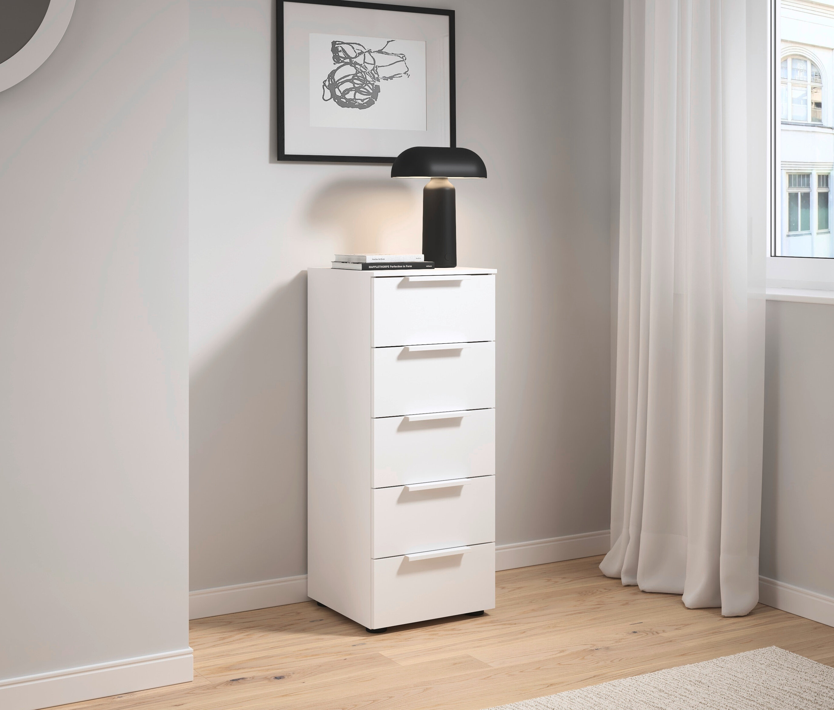 Weißer Schrank mit fünf Schubladen steht neben einer Wand mit einem Bild und einer Lampe.