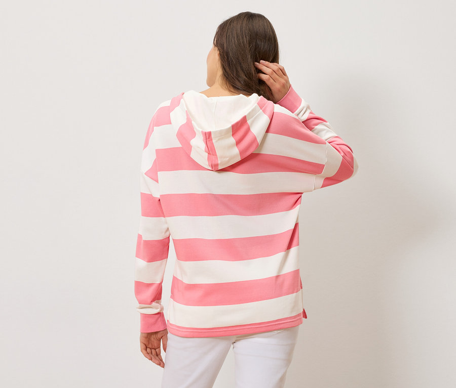 Frau von hinten, trägt einen gestreiften Hoodie in Rosa und Weiß und weiße Hosen.