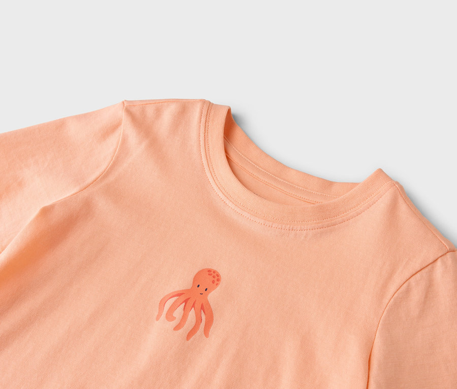 Nahaufnahme eines lachsfarbenen T-Shirts mit einem kleinen Tintenfisch-Motiv.