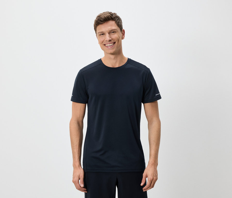 Ein Mann lächelt und trägt ein marineblaues T-Shirt und Shorts vor einem weißen Hintergrund.