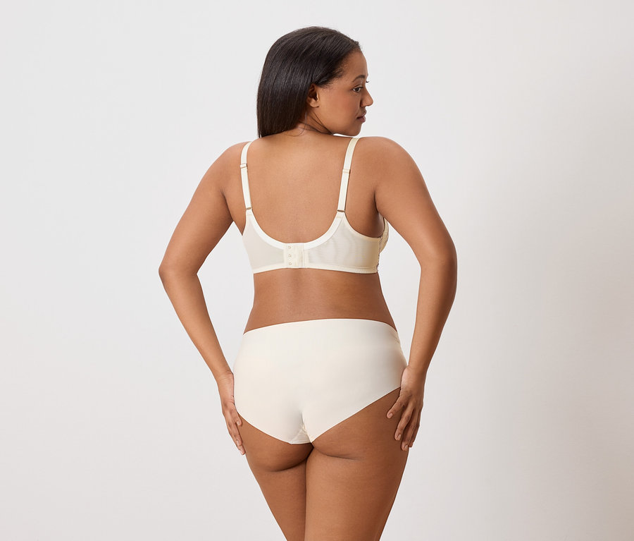 Dunkelhäutige Frau von hinten, trägt BH und Slip in Off-White.