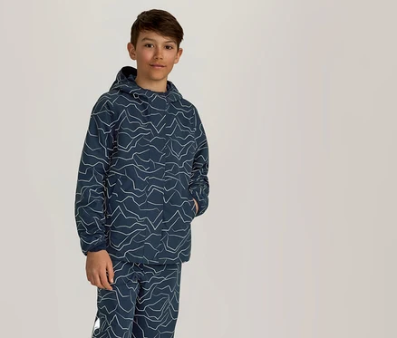 Ein Junge steht mit einer Hand in der Tasche in einem marineblauen Hoodie und einer Hose mit weißem Zickzackmuster.