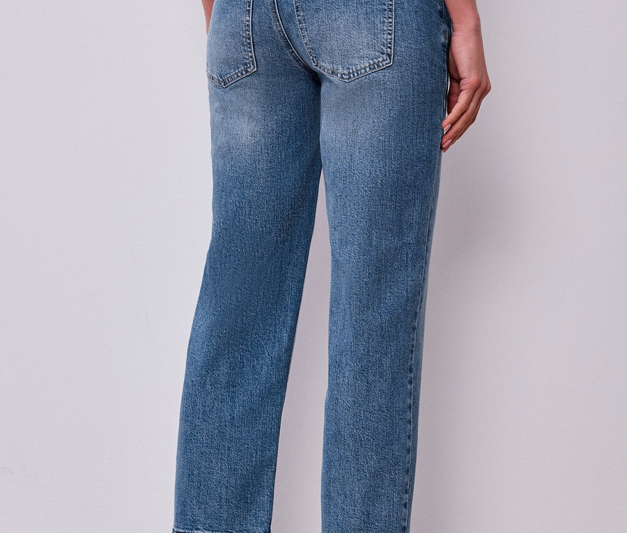 Person von hinten in blauer Street One Jeans mit ausgefranstem Saum und braunen Slippern.