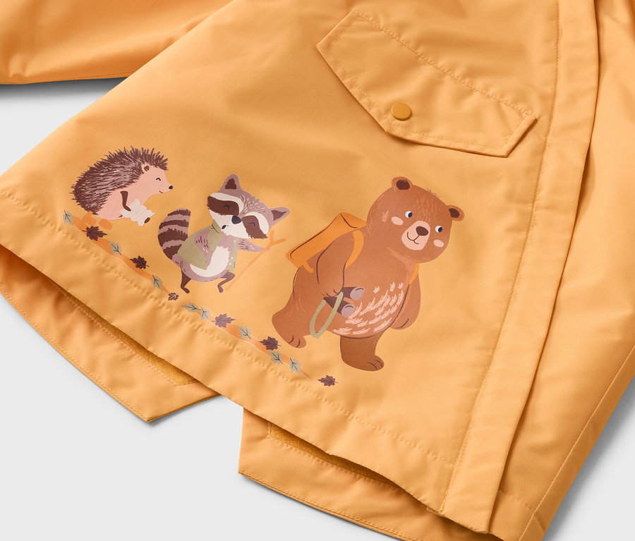 Nahaufnahme einer gelben Jacke mit aufgedrucktem Bär, Waschbär und Igel, die auf einem Ast stehen.