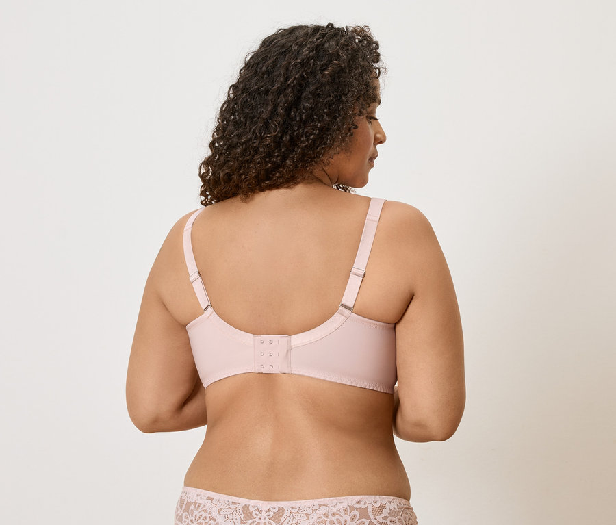 Rückansicht einer Frau mit lockigem Haar, die einen hellrosa BH und eine Unterhose mit Spitzenmuster trägt.