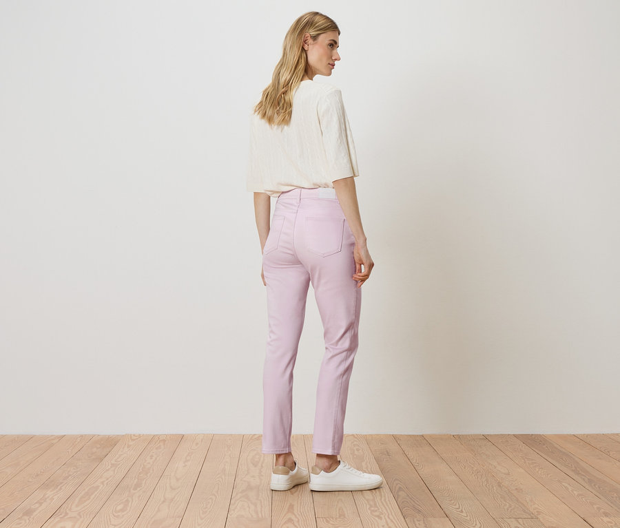 Eine Frau steht mit dem Rücken zur Kamera und trägt ein weißes Oberteil, eine rosa Hose und weiße Turnschuhe.