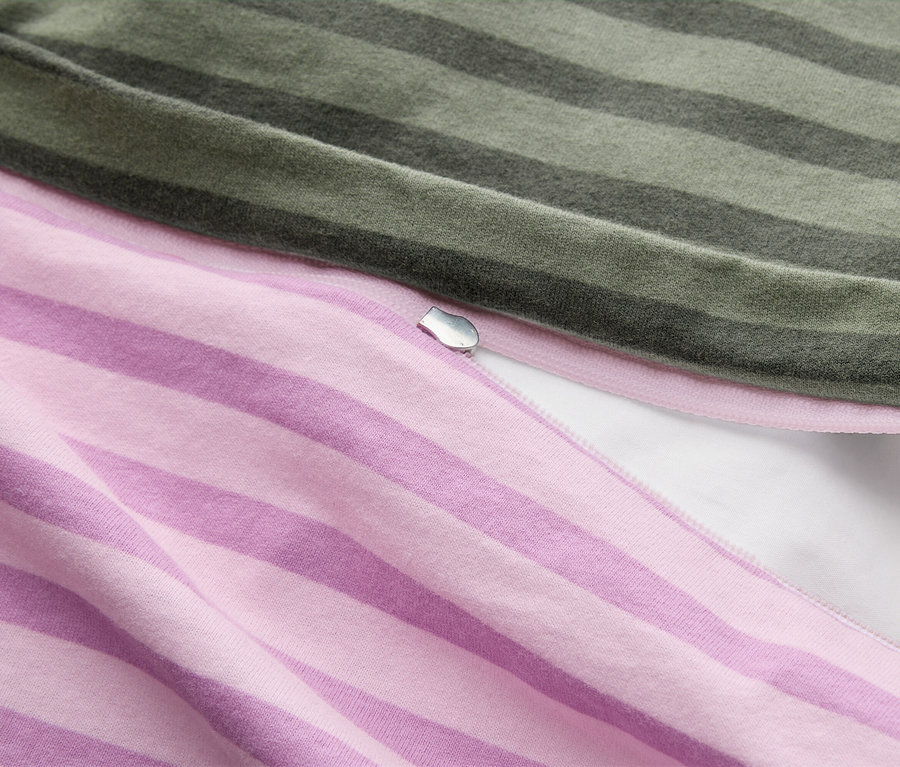 Nahaufnahme von zwei gestreiften Stoffen, einem grünen und einem rosa, mit einem silbernen Reißverschlusszipper dazwischen, der einen weißen Stoff darunter zeigt.