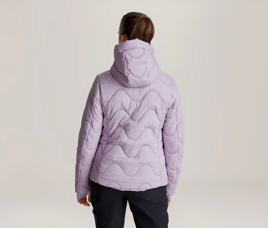 Frau von hinten in einer hellvioletten Steppjacke mit Kapuze und wellenförmigem Steppmuster, dazu schwarze Hose.