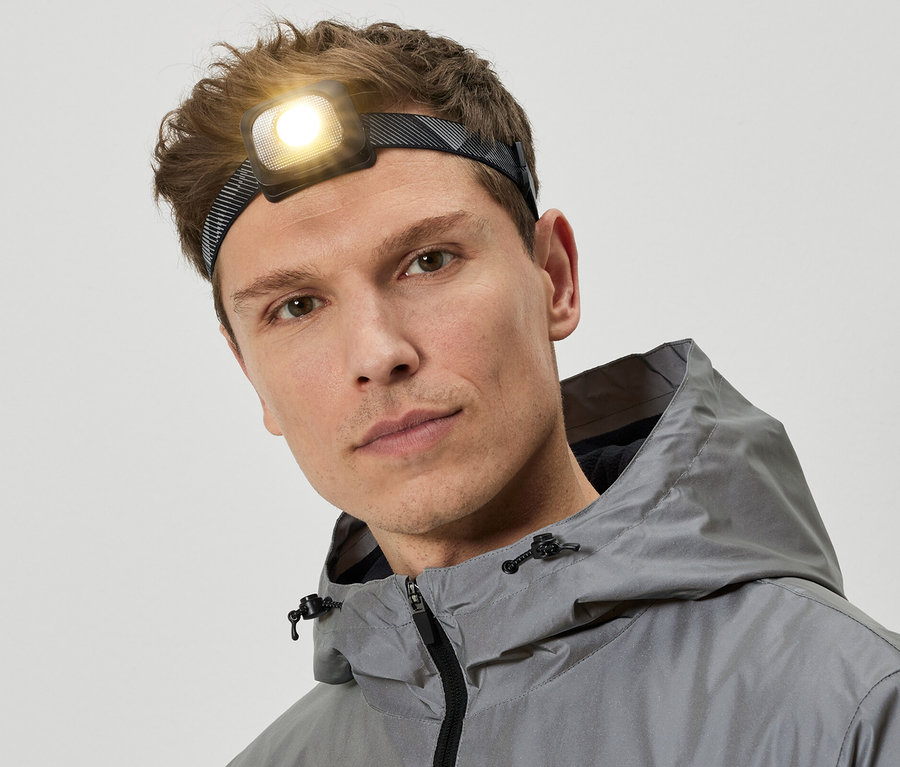 Mann mit Stirnlampe und grauer Kapuzenjacke.