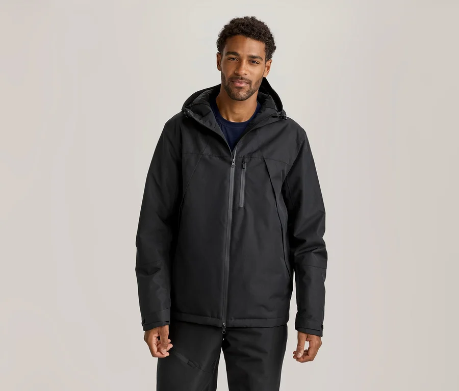 Mann trägt eine schwarze Kapuzenjacke über einem dunkelblauen T-Shirt und schwarze Hosen.