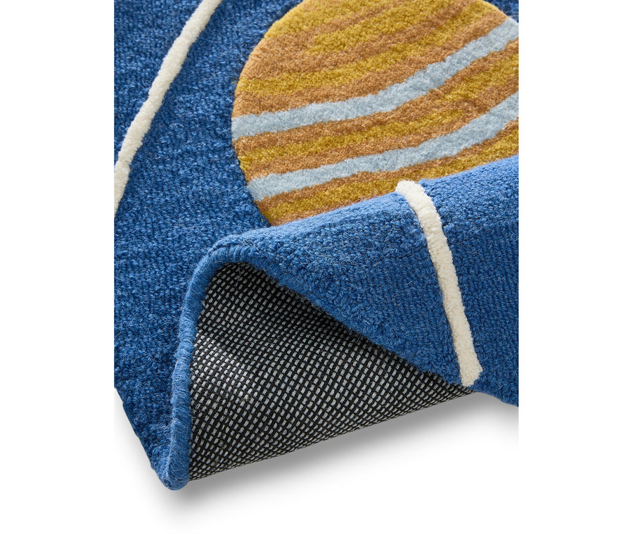 Ein blauer Teppich mit einem gelb-hellblau gestreiften Kreisdesign, teilweise aufgerollt, um seine schwarze, texturierte Unterseite zu zeigen. Weiße Linien sind ebenfalls auf der blauen Oberfläche sichtbar.