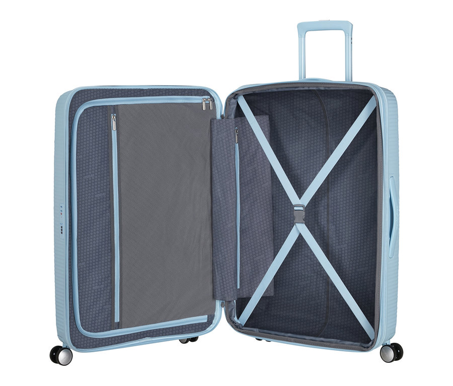 Ein geöffneter, großer, pastellblauer American Tourister Hartschalen-Koffer »Soundbox« Spinner mit Netzfach und Kreuzspanngurten.