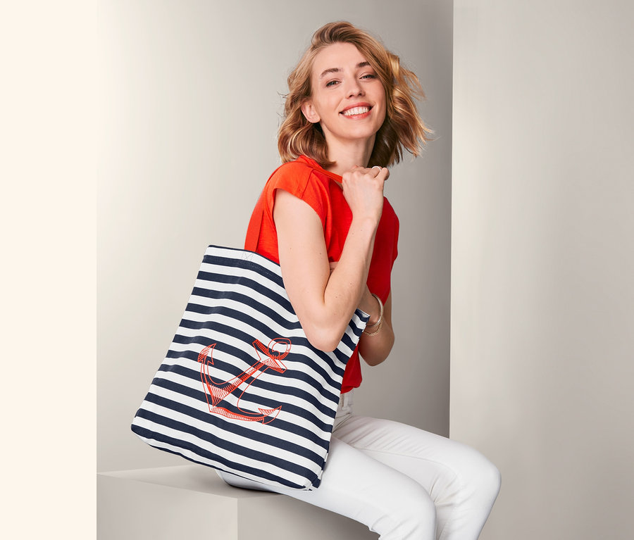 Frau sitzt und hält eine gestreifte Tasche mit einem Ankermotiv.