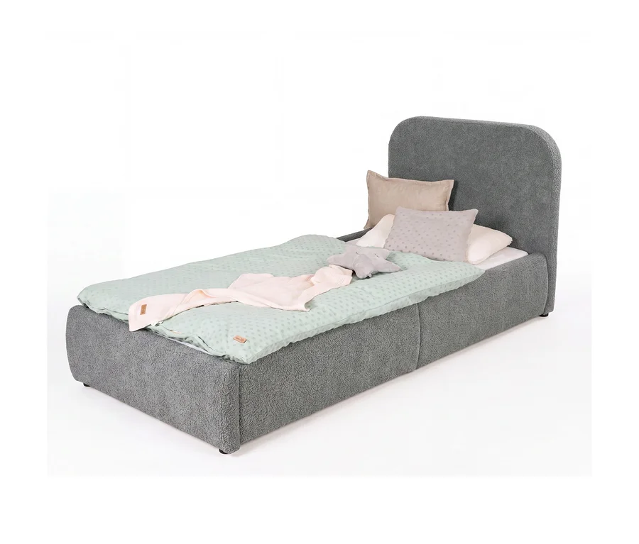 Graues Einzelbett mit abgerundetem Kopfteil, bezogen mit hellgrüner gepunkteter Bettwäsche, einer rosa Decke und mehreren Kissen, darunter ein sternförmiges Kissen.
