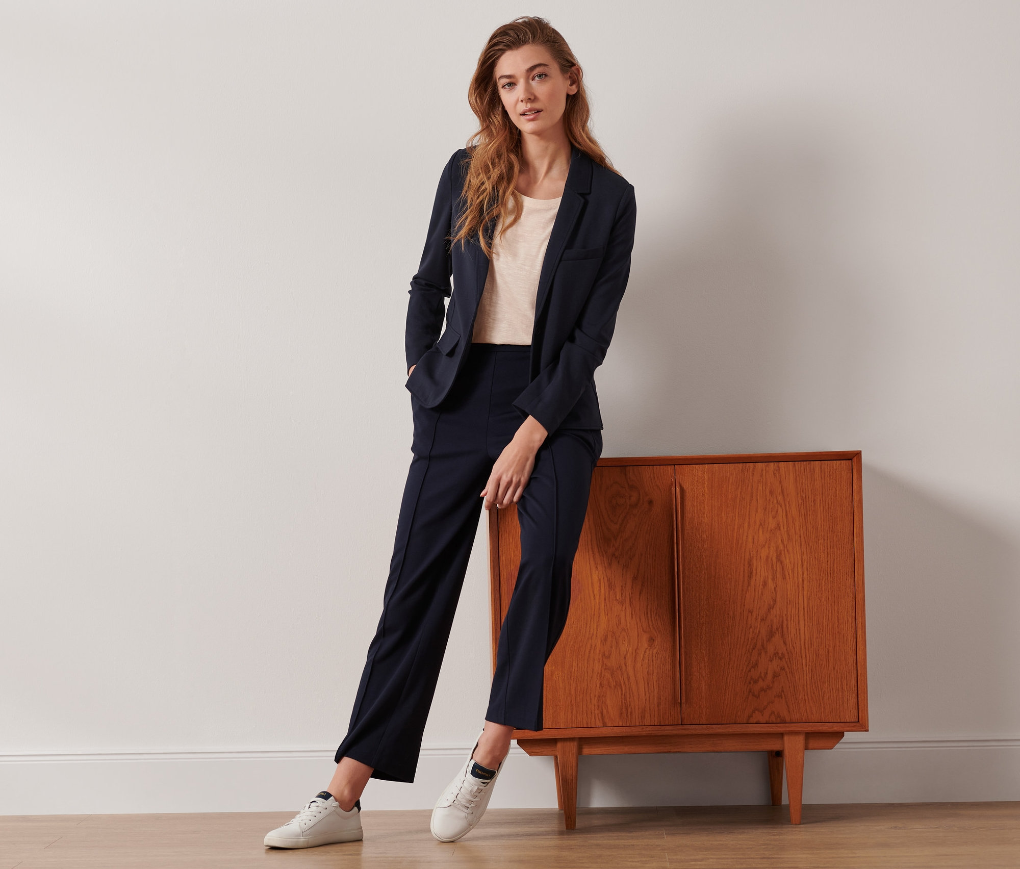 Eine Frau posiert an einem Schrank gelehnt in einem Jerseyblazer und einer dunkelblauen Jerseyhose mit Biese.