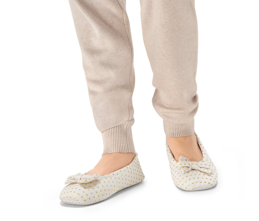 Beine in beigen Hosen und Ballerina-Hausschuhen.