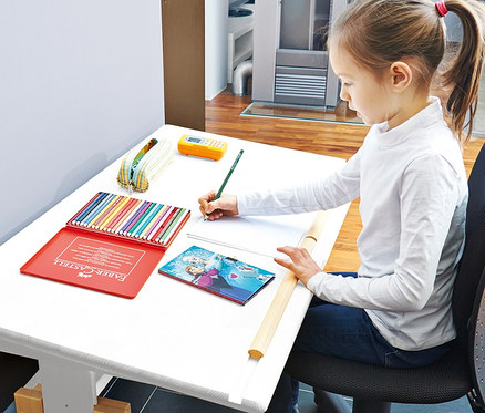 Mädchen sitzt an höhenverstellbarem Pinolino Kinderschreibtisch „Lena“ und zeichnet mit Buntstift auf Papier.