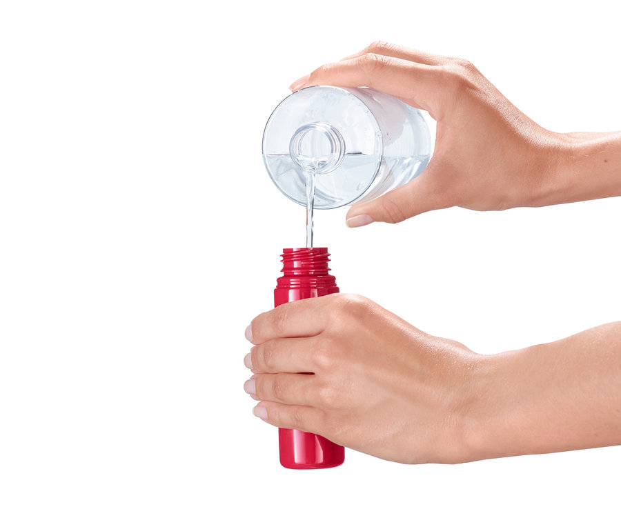 Flüssigkeit wird aus einem klaren Behälter in einen roten Desinfektionsstift gegossen.