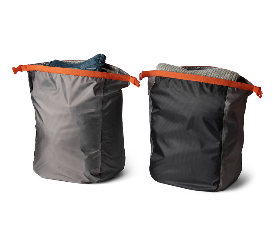 Zwei wasserfeste Packsäcke mit orangefarbenen Details, einer mit einer Jeansjacke und der andere mit einem grauen Pullover.