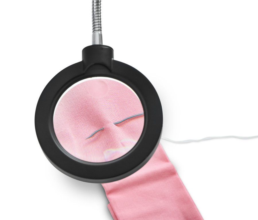 Nahaufnahme einer Handarbeitslampe mit Lupe, die einen rosa Stoff mit einer Nadel beleuchtet.