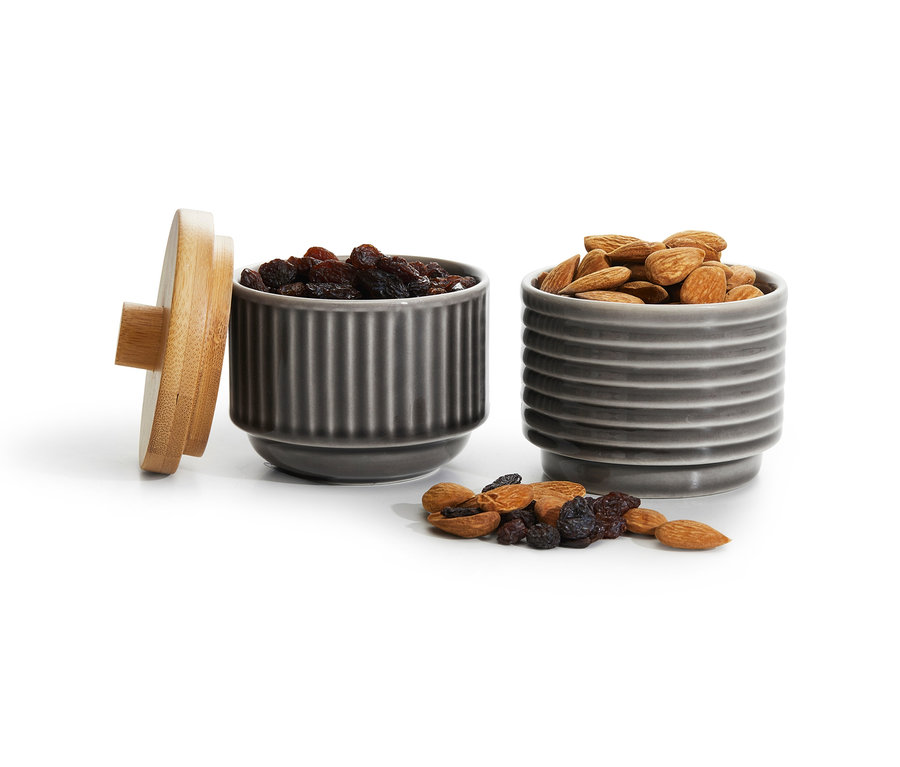 Zwei graue Servierschalen, eine mit Rosinen, eine mit Mandeln und ein Holzdeckel.