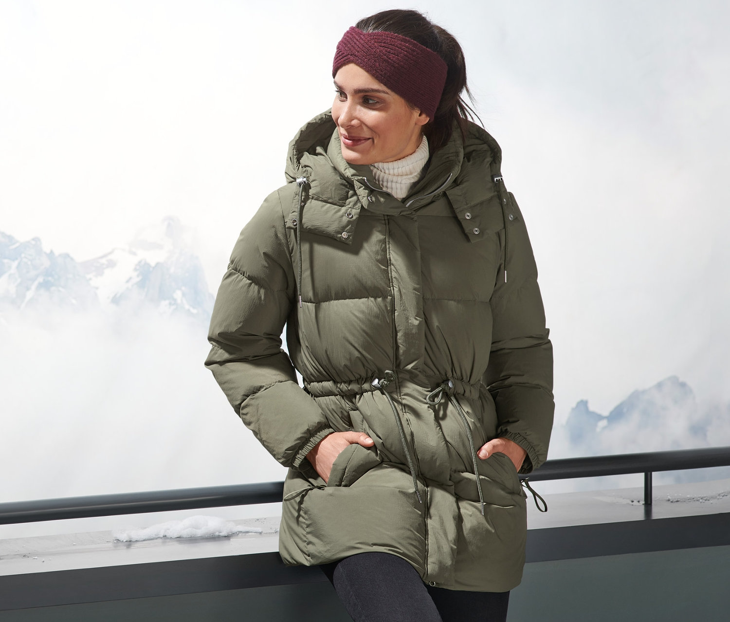 Frau mit Daunenjacke steht draußen mit Bergen im Hintergrund.