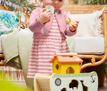 Kleinkind spielt mit dem small foot Steckspiel »Arche Noah Safari«, trägt ein Baby-Jerseykleid und eine Baby-Bolero-Jacke.