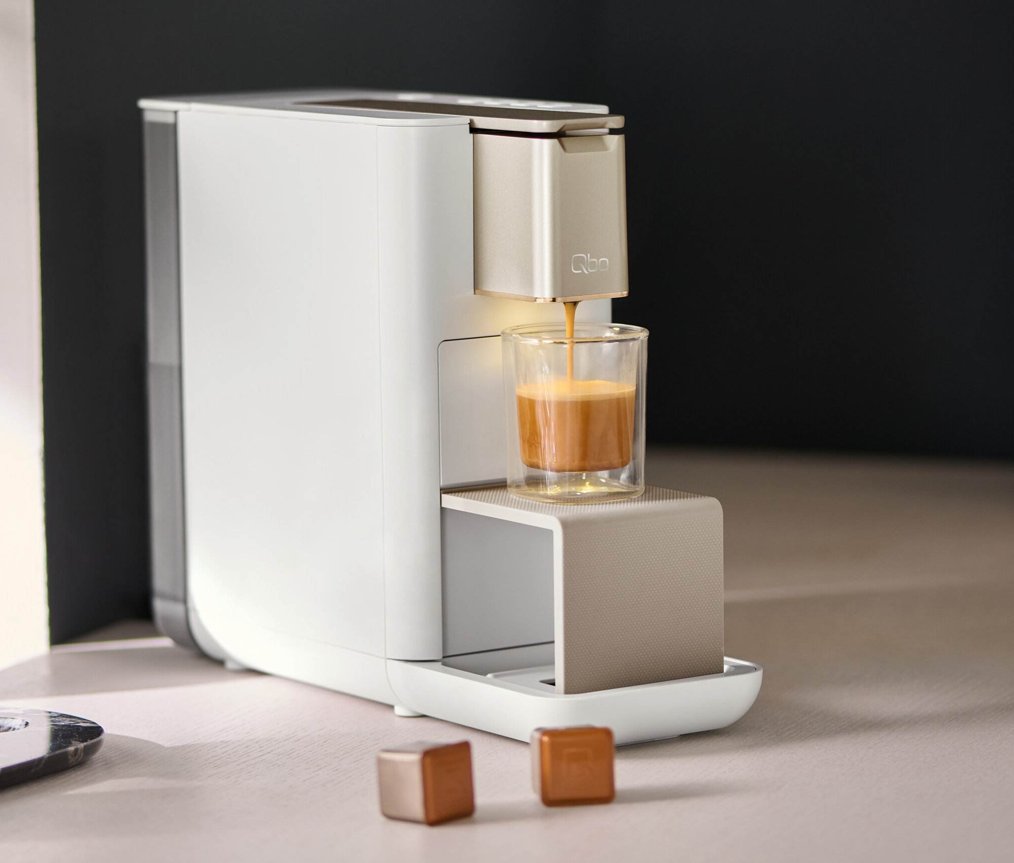 Qbo ICONIC Light Gold Kaffeemaschine füllt Kaffee in ein Glas.