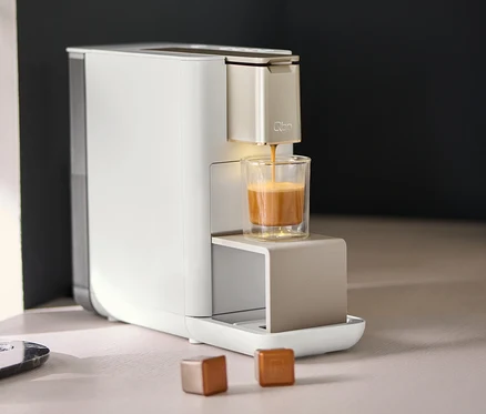 Qbo ICONIC Light Gold Kaffeemaschine füllt Kaffee in ein Glas.