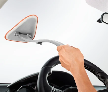 Eine Hand hält einen Autoscheibenreiniger und reinigt die Windschutzscheibe eines Autos.