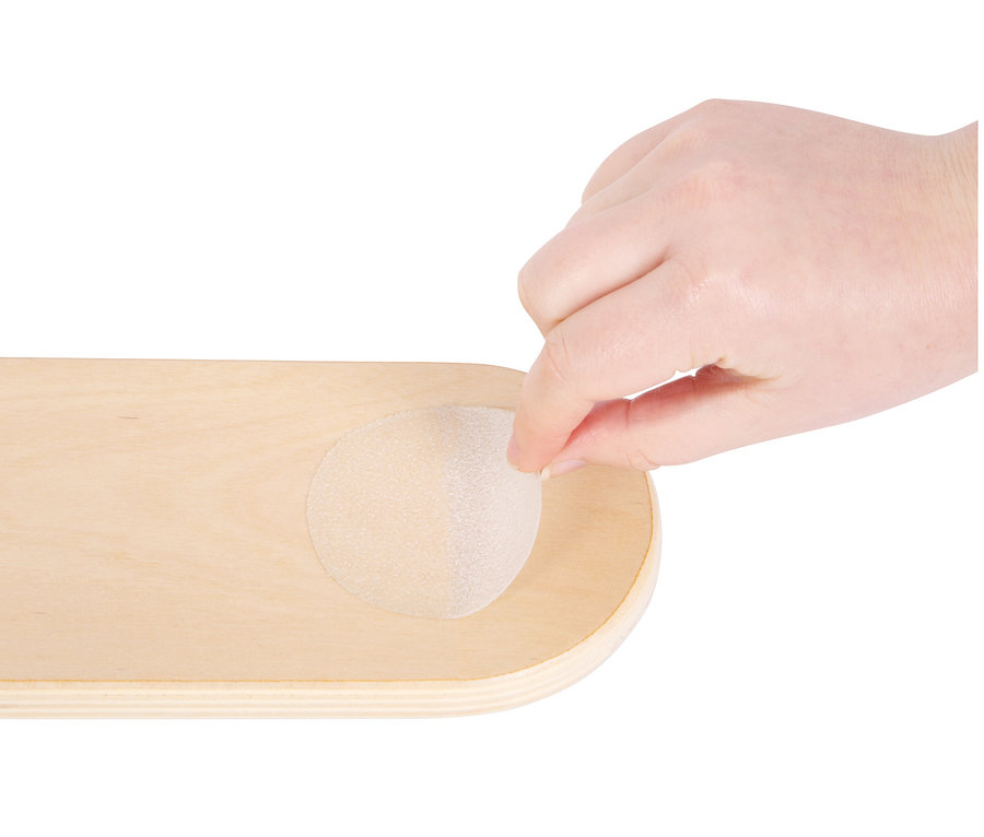 Eine Hand platziert einen kleinen small foot Balancierstein »Adventure« auf einem Holzbrett.