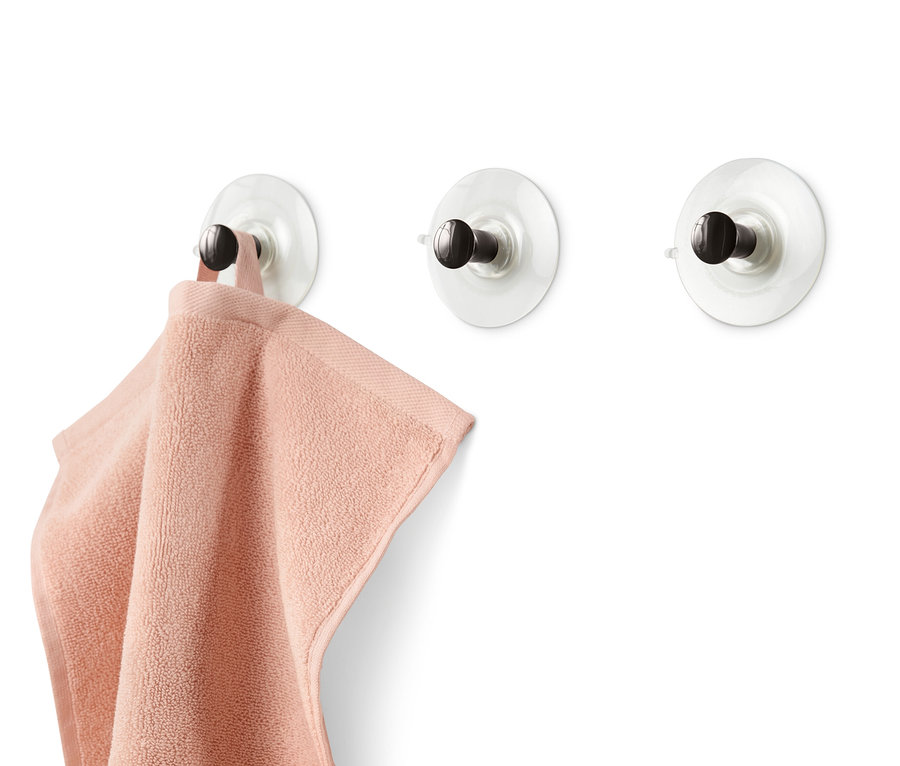 Drei Haken mit Saugnapf sind an einer weißen Wand befestigt, an einem davon hängt ein rosa Handtuch.