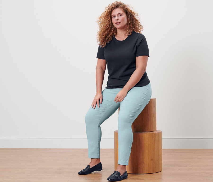 Frau sitzt auf Holzstufen und trägt ein dunkelblaues Basic T-Shirt und eine Stretchhose.