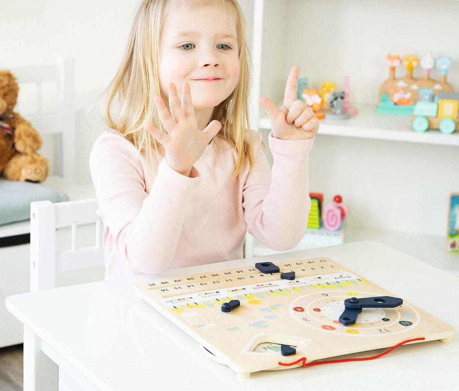 Mädchen zeigt mit Fingern die Zahl Sieben an einer hölzernen Lernuhr mit Kalender »Educate«.