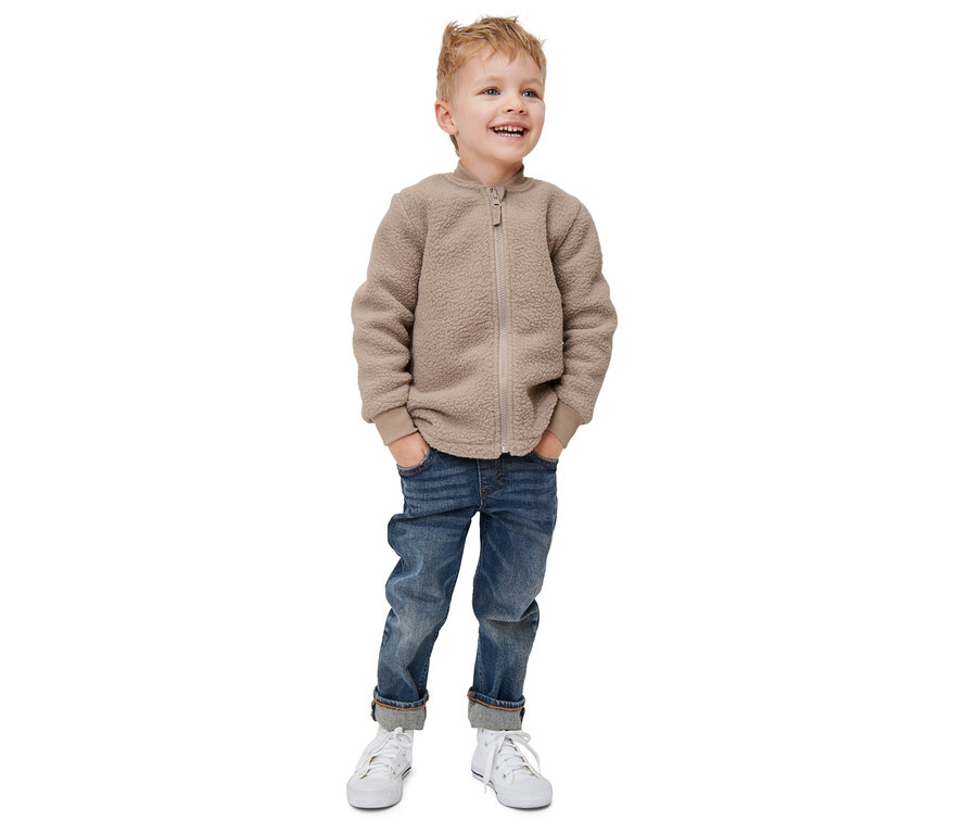 Ein Junge trägt eine Kleinkind-3-in-1-Outdoorjacke, Jeans und Turnschuhe.