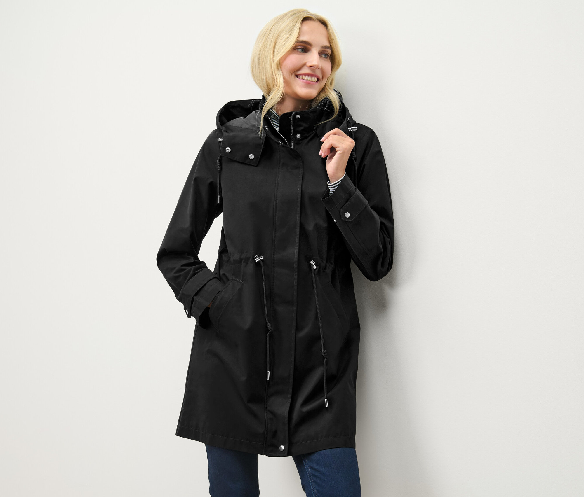 Blonde Frau posiert in schwarzem Parka mit Kapuze.