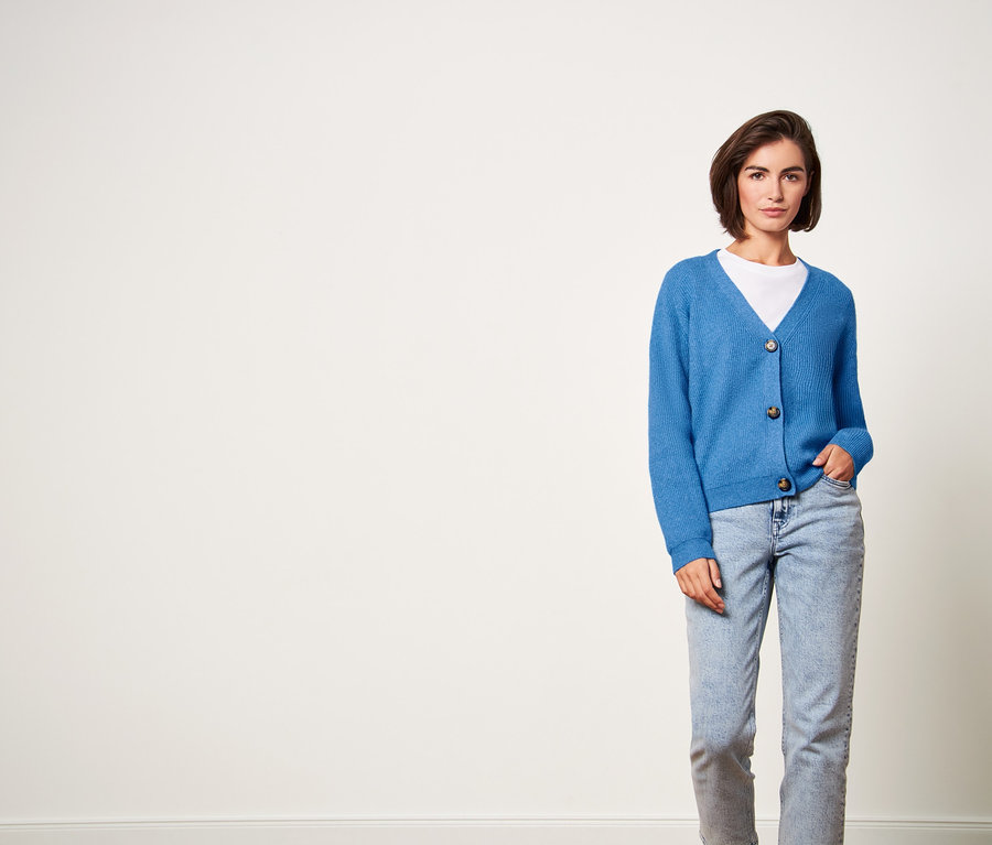 Frau posiert in blauem Grobstrick-Cardigan, Jeans und weißem T-Shirt.