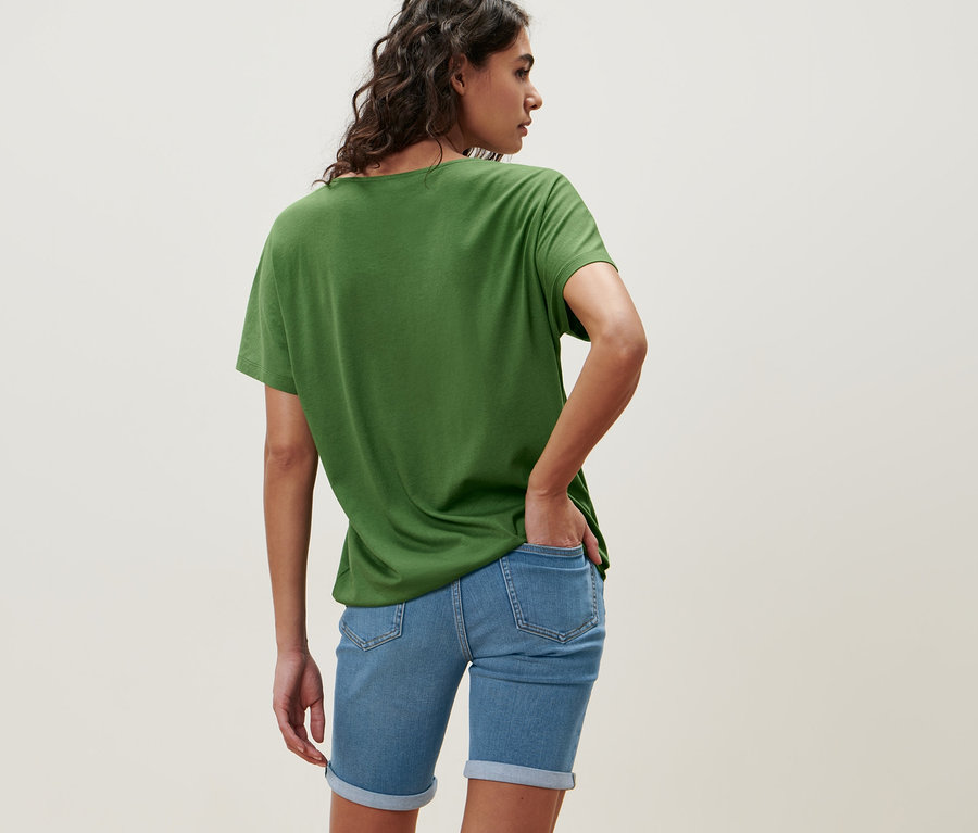 Frau trägt ein grünes Blusenshirt und Jeansshorts.