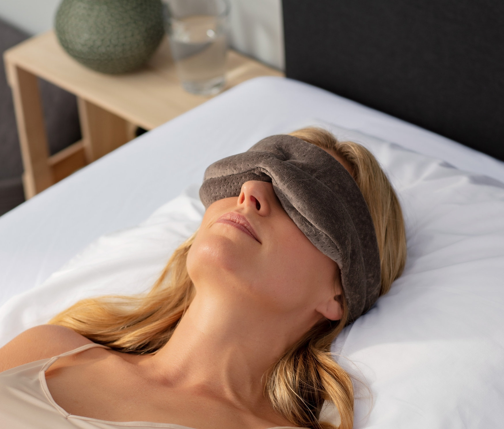 Frau liegt im Bett mit einer braunen TEMPUR® Schlafmaske auf den Augen.