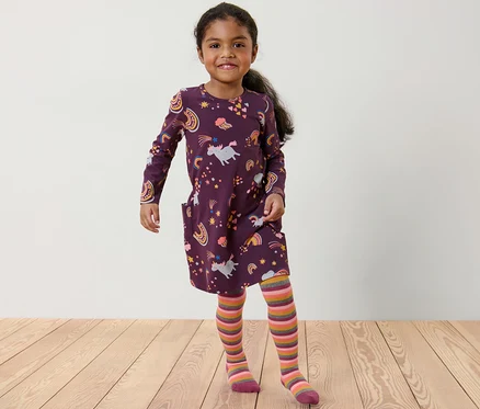 Lächelndes Mädchen posiert in einem lila Einhornkleid und einer auberginefarbenen Thermostrumpfhose mit bunten Streifen.