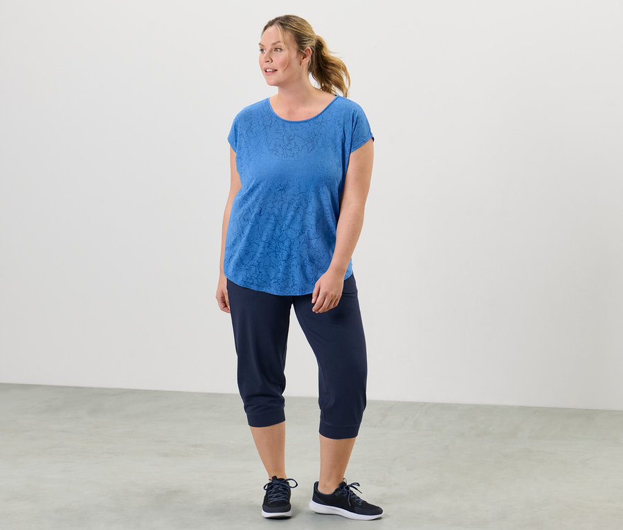 Frau steht und trägt ein blaues Sportshirt.