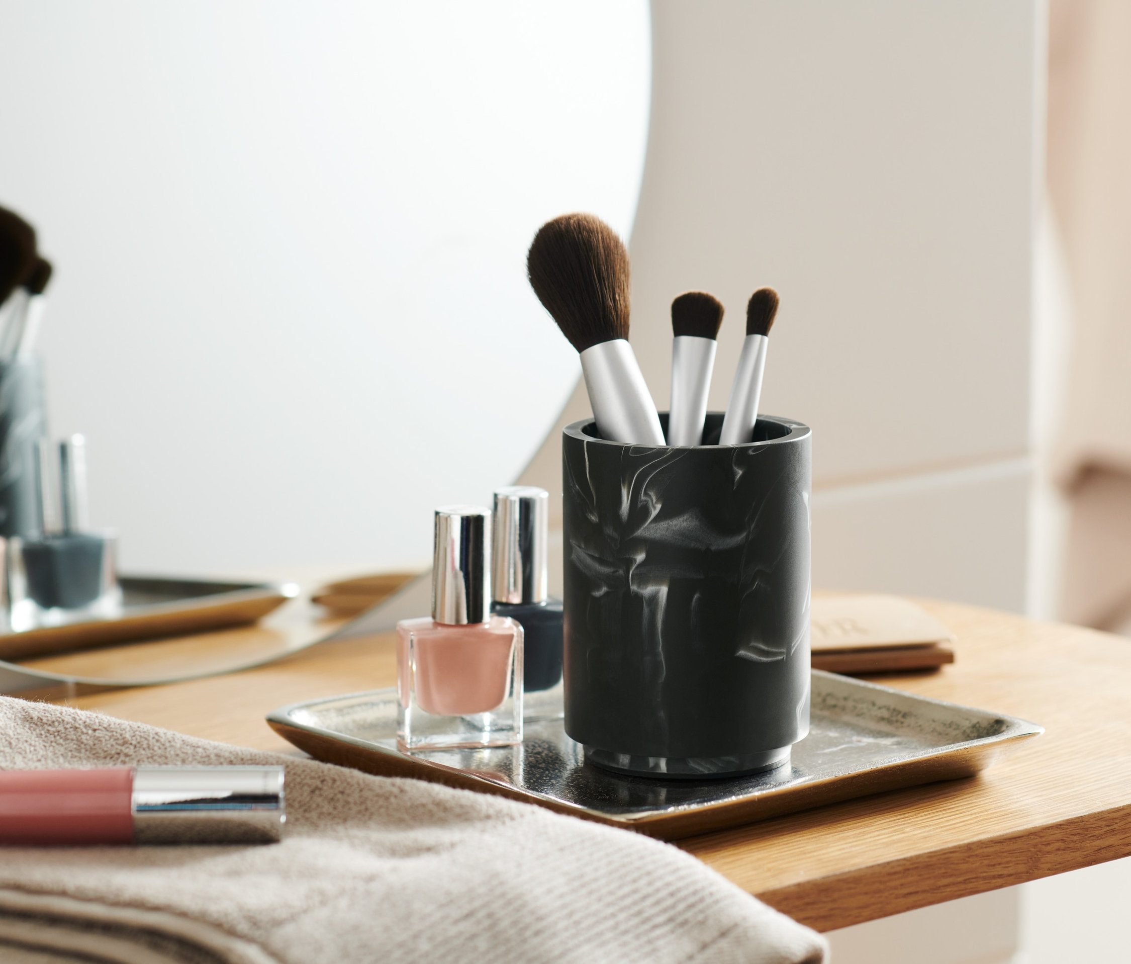 Make-up Pinsel in marmoriertem Utensilo neben Nagellacken auf einem Tablett.