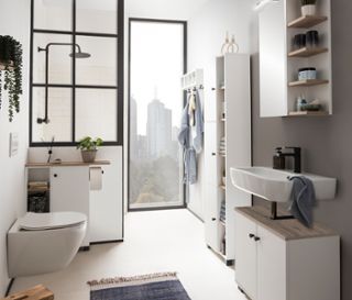 Ein Badezimmer mit Toilette, Duschkabine und einem Waschtisch mit dem »Balto« Waschbeckenunterschrank, Badschrank, Hochschrank und Regal in mattem Weiß.