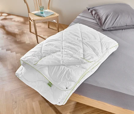 Ein weißes irisette® greenline 4-Jahreszeiten-Steppbett liegt auf einem Bett.